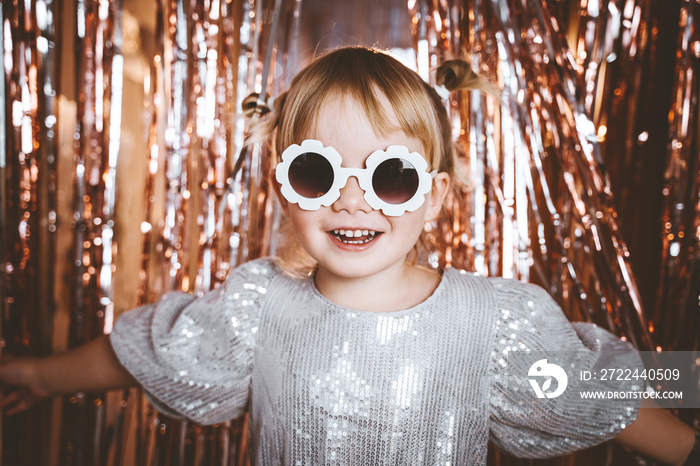 Portrait of happy little girl in dress and sunglasses having fun on the festive background. Kids birthday or fancy dress party, disco music or New Year. Celebration and Holiday concept.