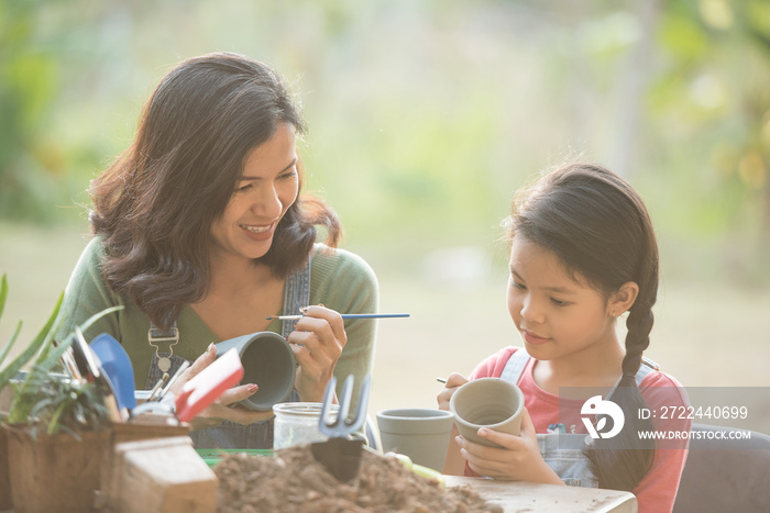 adorable asian little girl are painting potted plants made of pottery in garden outside house, caring for new life. earth day holiday concept. world environment day. ecology.