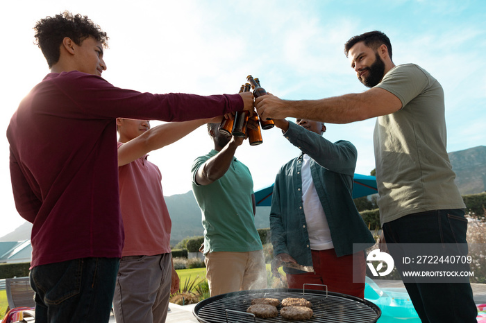 Low angle view of multiracial male friends toasting beer bottles while having fun at barbecue party