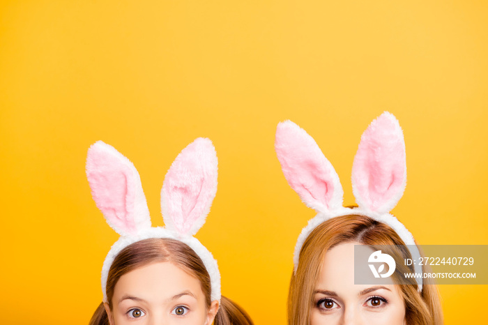 Cropped close up half-faced portrait photo of excited cheerful beautiful mom and small sweet playful funny lovely tender daughter wearing bunny ears isolated on yellow background