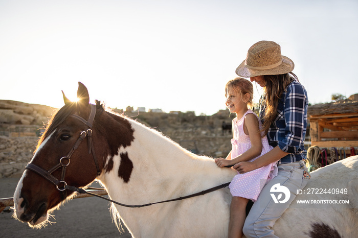 Happy mother and daughter riding a horse at sunset - Family people lifestyle and love concept - Focus on kid face