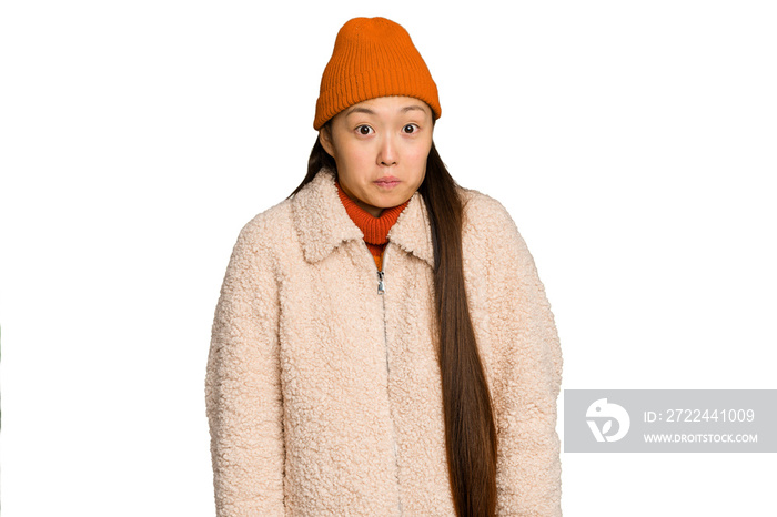 Young asian woman wearing winter clothes isolated on green chroma background shrugs shoulders and open eyes confused.