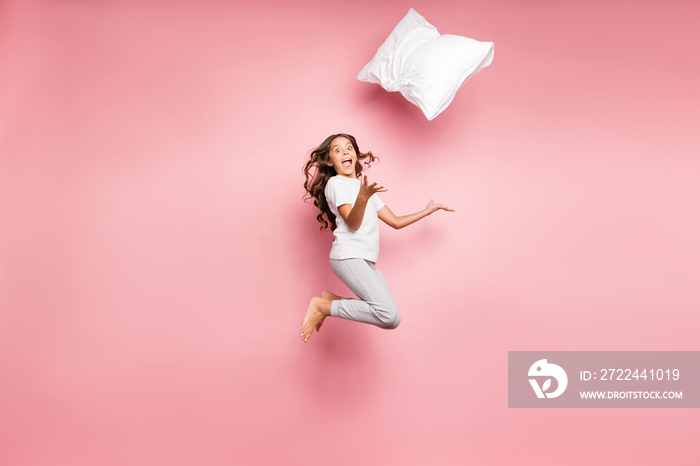 Full length body size turned photo of cheerful crazy barefoot amazed child throwing her pillow up expressing excitement on face jumping up isolated pastel color background