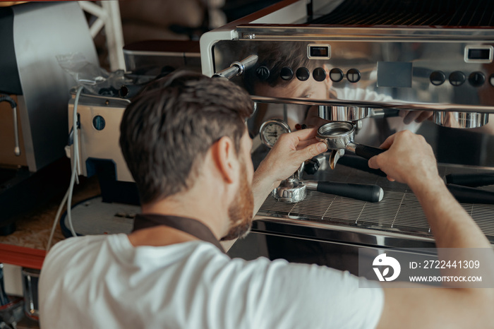 Man worker in uniform inspecting coffee machine in own workshop