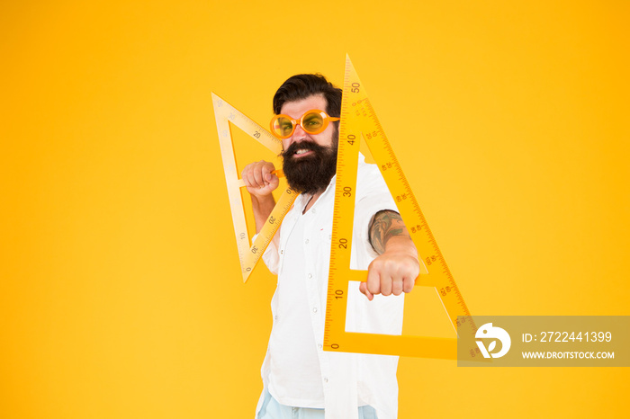 Math genius. Geometry geek holding triangles on yellow background. Geek or nerdy student making angle. Bearded man in fancy geek glasses making technical drawing. Being a geek is extremely liberating