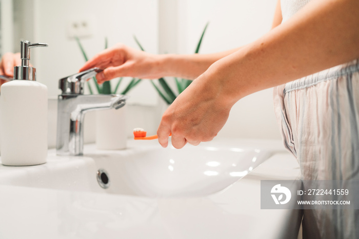 Close up unrecognizable woman opening the faucet to wet her toothbrush