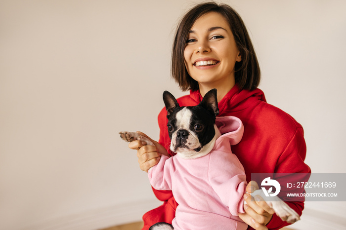 Cheerful young european female model resting with boston terrier in front of white background. Girl enjoying portrait photography with her cute pet. Dog care concept.