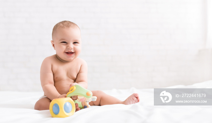 Cute newborn baby playing with toys on bed