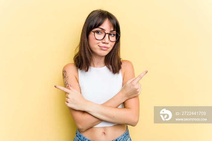 Young caucasian woman isolated on yellow background points sideways, is trying to choose between two options.