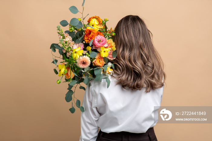 people and floral design concept - woman with bunch of flowers over beige background from back