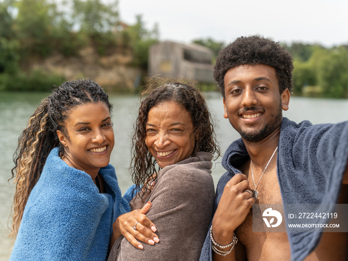 Portrait of smiling friends wrapped in towels by lake