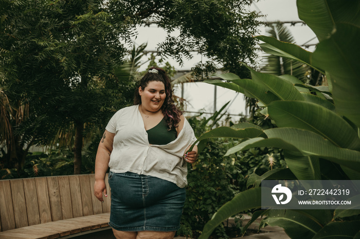 plus size woman walks through park with tropical plants