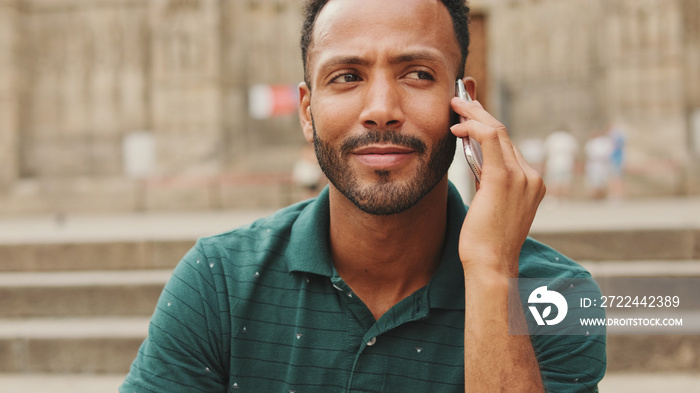 Happy young man sits on the steps of the Sagrada Familia in Barcelona, talking on smartphone