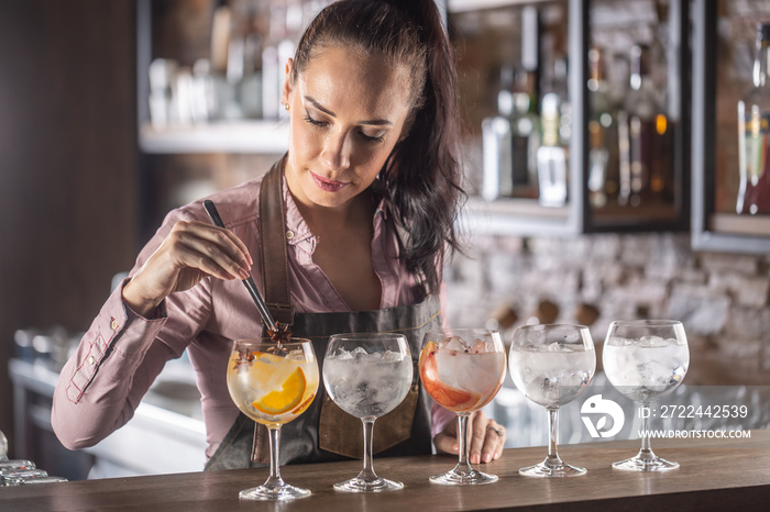 Barmaid is preparing a selection of five various gin tonic drinks on the bar