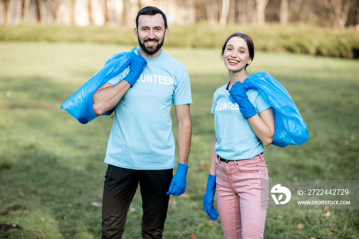 Portrait of a happy volunteers in blue t-shirts standing with bags full of rubbish after the park cleaning