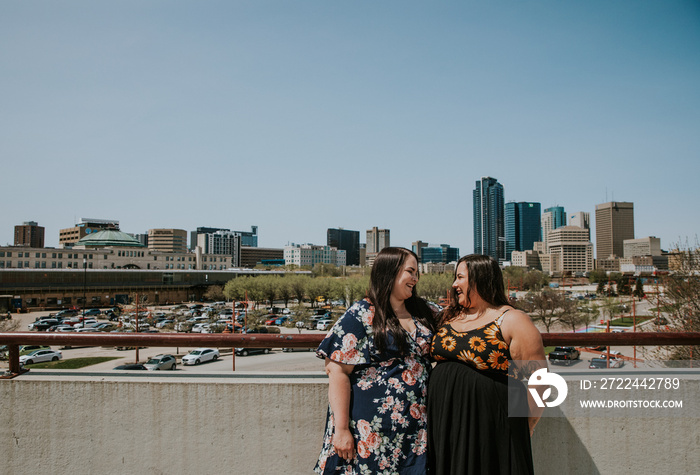 2 women stand on a rooftop overlooking the city