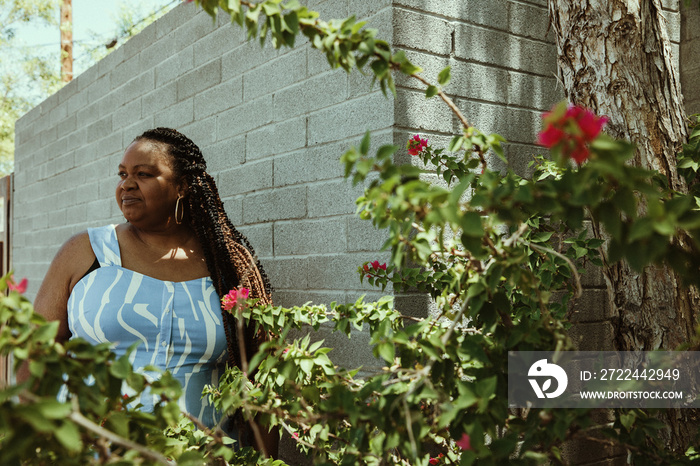 Plus size afro latinx Haitian American woman stands against wall surrounded by flowers