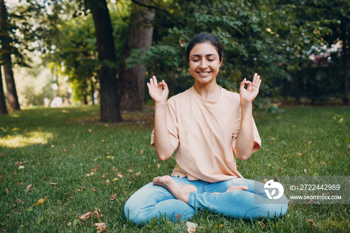 Indian woman doing yoga and meditation in lotus asana pose in outdoor summer park.