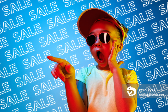 Portrait of young caucasian girl in sunglasses on blue background with neon lettering. Concept of sales, black friday, cyber monday, finance, business. Online shops and payments bill.