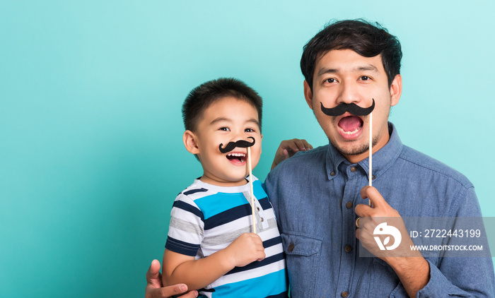 Family funny happy hipster father and his son kid holding black mustache props for the photo booth close face, studio shot isolated on a blue background, November men health awareness