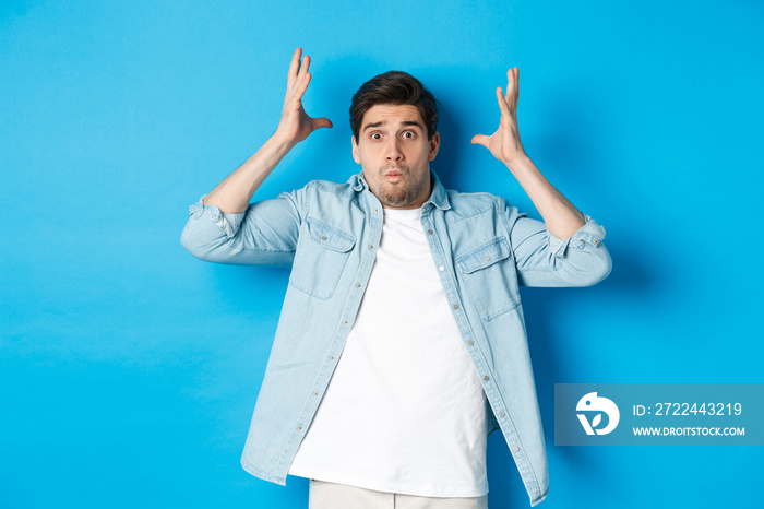 Distressed guy showing mind blowing gesture, looking frustrated and anxious, standing against blue background