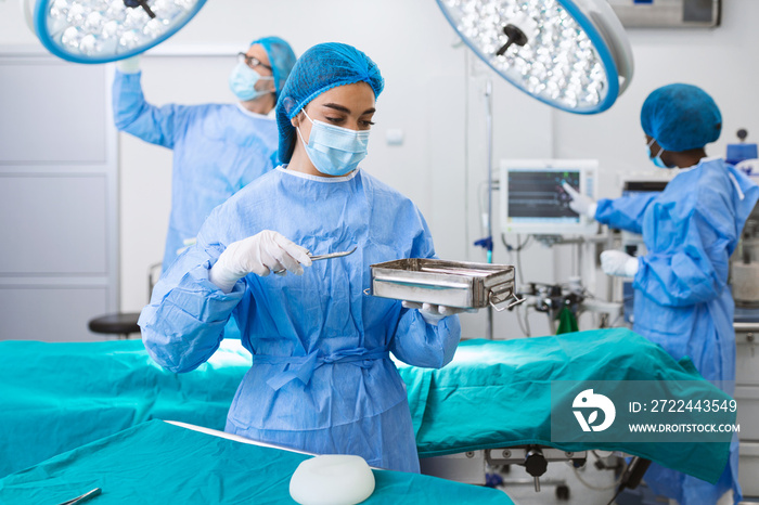 Female surgeon in surgical uniform taking surgical instruments at operating room. Young woman doctor in hospital operation theater