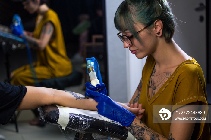 Tattoo artist demonstrates the process of getting black tattoo with paint. Master works in blue sterile gloves. Master of tattoo fill circuit tattoo.