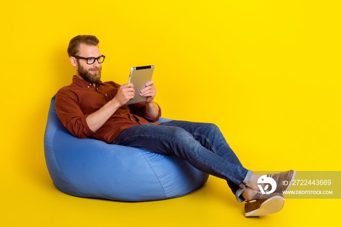 Full body photo of intelligent man sit cozy bag use tablet typing chatting isolated on yellow color background