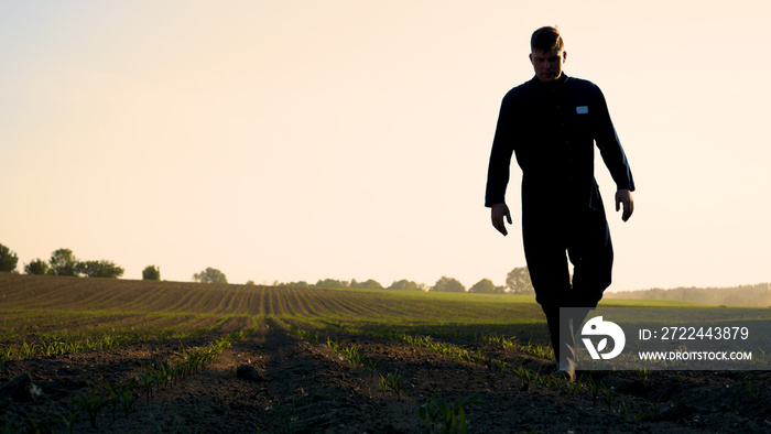 A young farmer in a blue robe walks the field looking at planted plants. Concept: clean air, bio, agriculture.