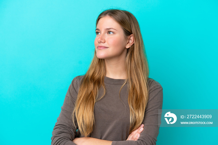 Young blonde woman isolated on blue background looking to the side