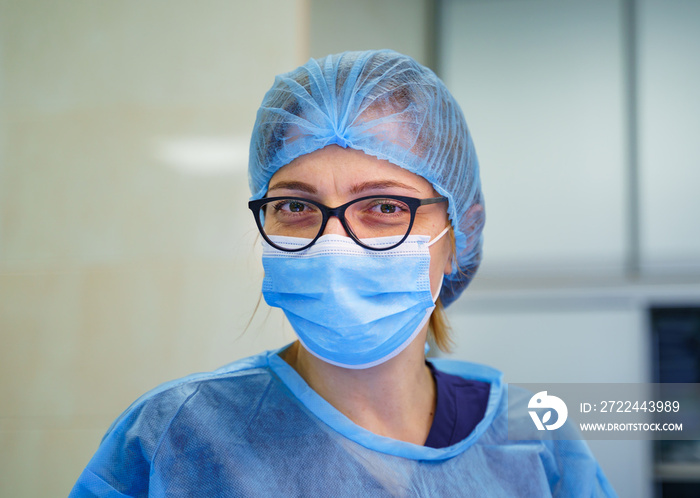 Doctor or nurse smiling behind surgeon mask. Closeup portrait of young woman model in blue medical scrub. Coronovirus epidemic. Ambulance station. Intensive care unit with Pneumonia diagnosting.