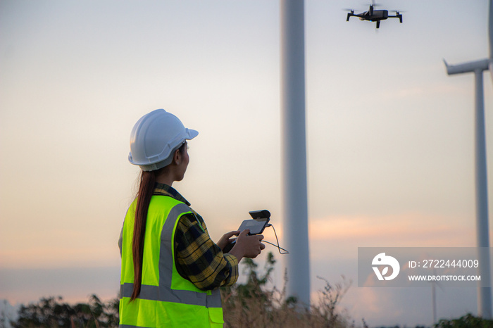 asian female engineer using drone for  inspection wind turbine farm in evening.