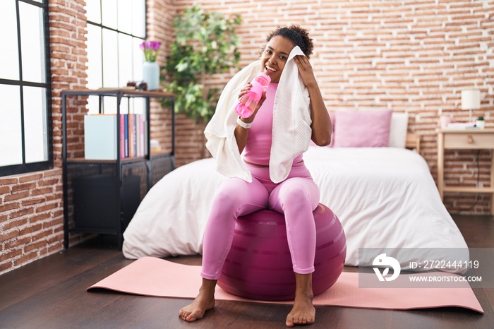 African american woman drinking water using towel at bedroom