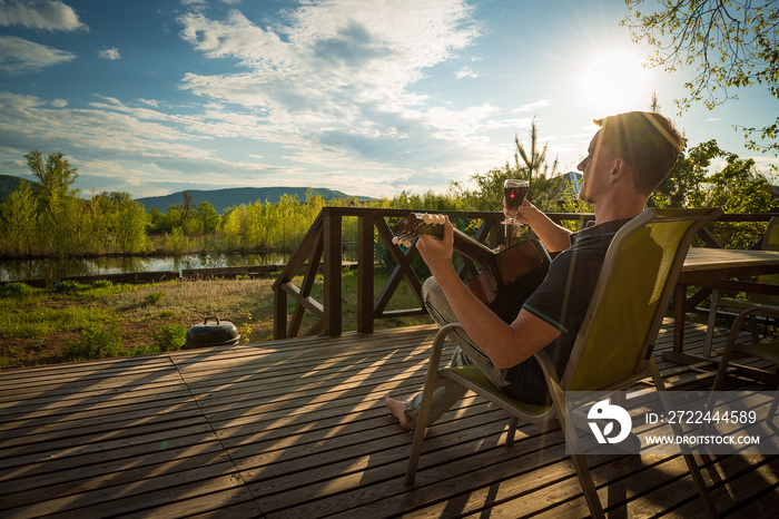 Young man playing guitar and drinking wine alone. Covid-19 quarantine.