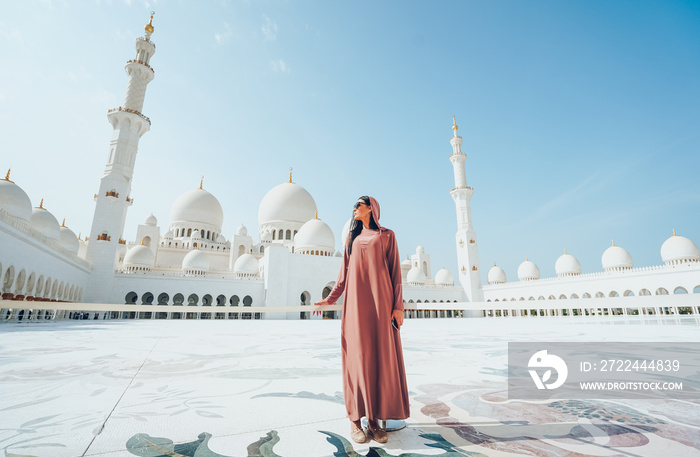 A young girl in hijab stands against the background of the abu dhabi mosque.