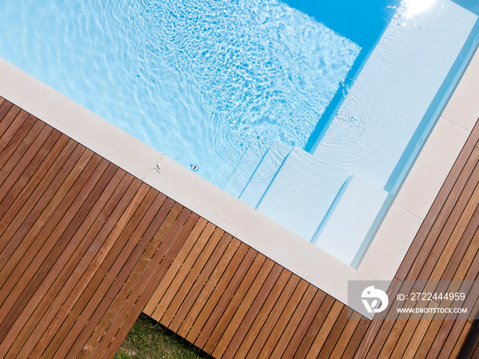 Drone flight over pool with nice wooden terrace surrounded by green lawn in beautiful garden