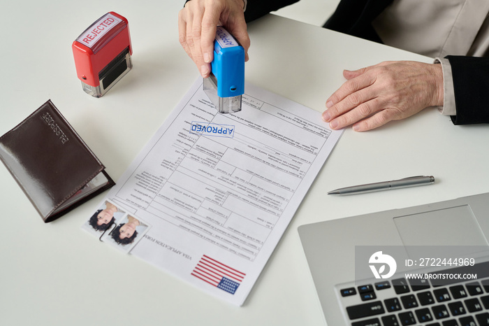 Close up of unrecognizable worker putting approved stamp on visa application form in US immigration office