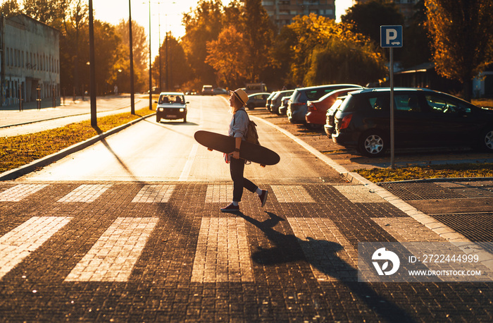 Portrait of smiling girl with long board in the city during sunset.