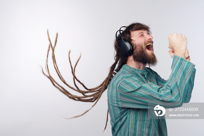 Young rastafarian reggae culture man with dreadlocks dancing to the music he’s listening to on his big headphones, studio background