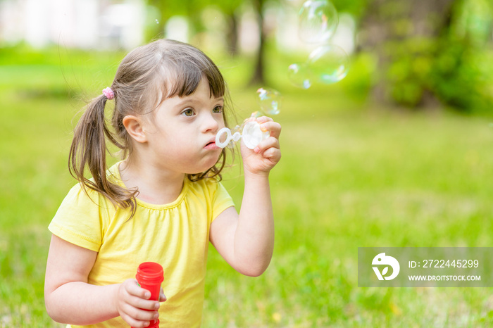 Little girl with syndrome down blows bubbles in a summer park