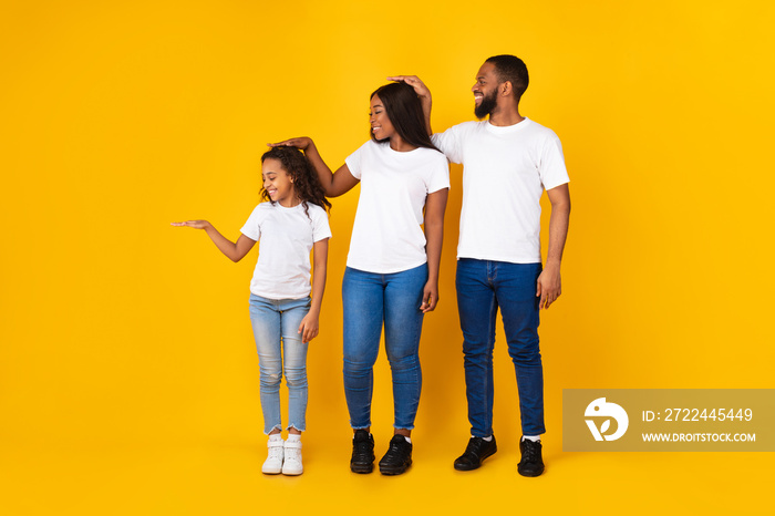 African American man, woman and daughter measuring height