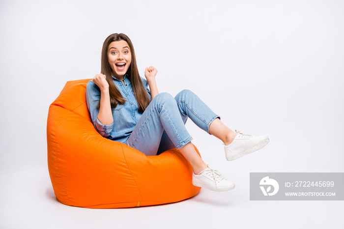 Full length photo of funky funny girl sit on lounge chair watch football match impressed about team victory raise fists scream omg wear casual style outfit sneakers isolated white color background