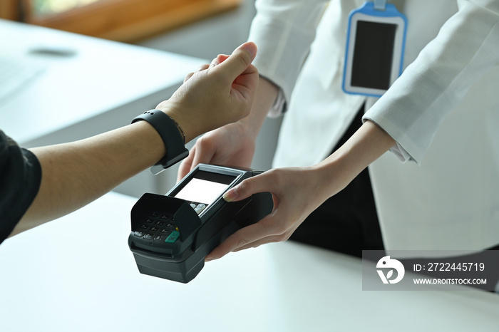 Cropped image of a young man using a smartwatch for doing a payment at the automatic payment machine.