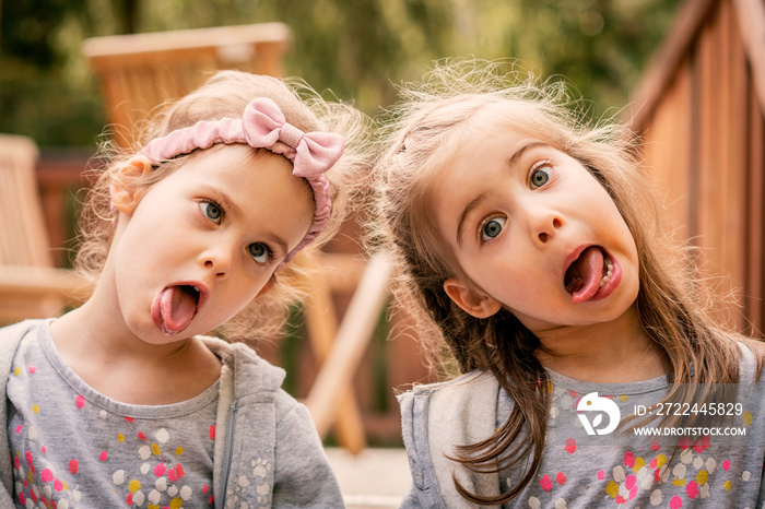 two adorable girls are sitting on the stairs and making funny faces