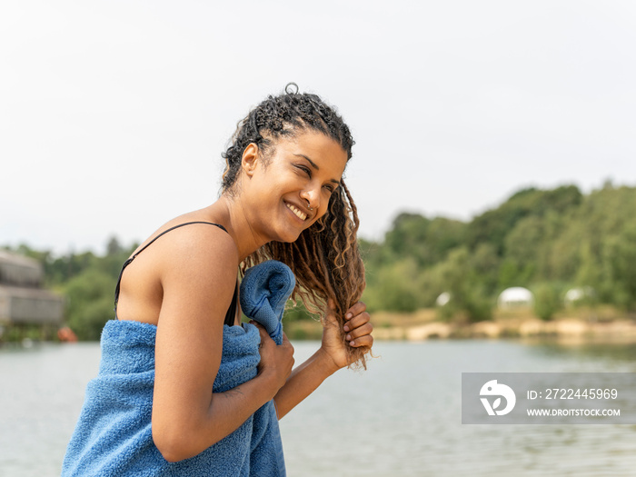 Smiling woman standing wrapped in towel by lake