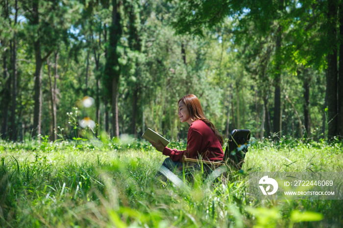 Portrait of a beautiful young asian woman reading a book while sitting on a camping chair in the park