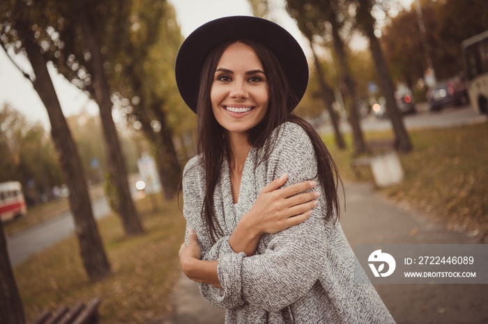 Photo portrait of pretty girl smiling embracing herself in cold autumn weather on city streets wearing grey casual outfit