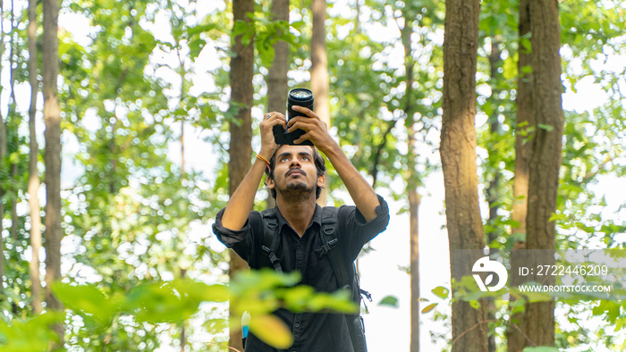 Young photographer standing in the nature, taking picture with professional camera