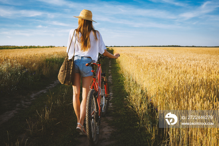 Girl in wheat summer field with bicycle