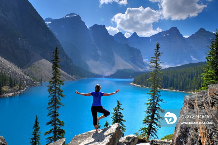 Woman in yoga pose at alpine lake and mountains. Moraine Lake in Rocky Mountains. Banff National Park, Alberta, Canada.